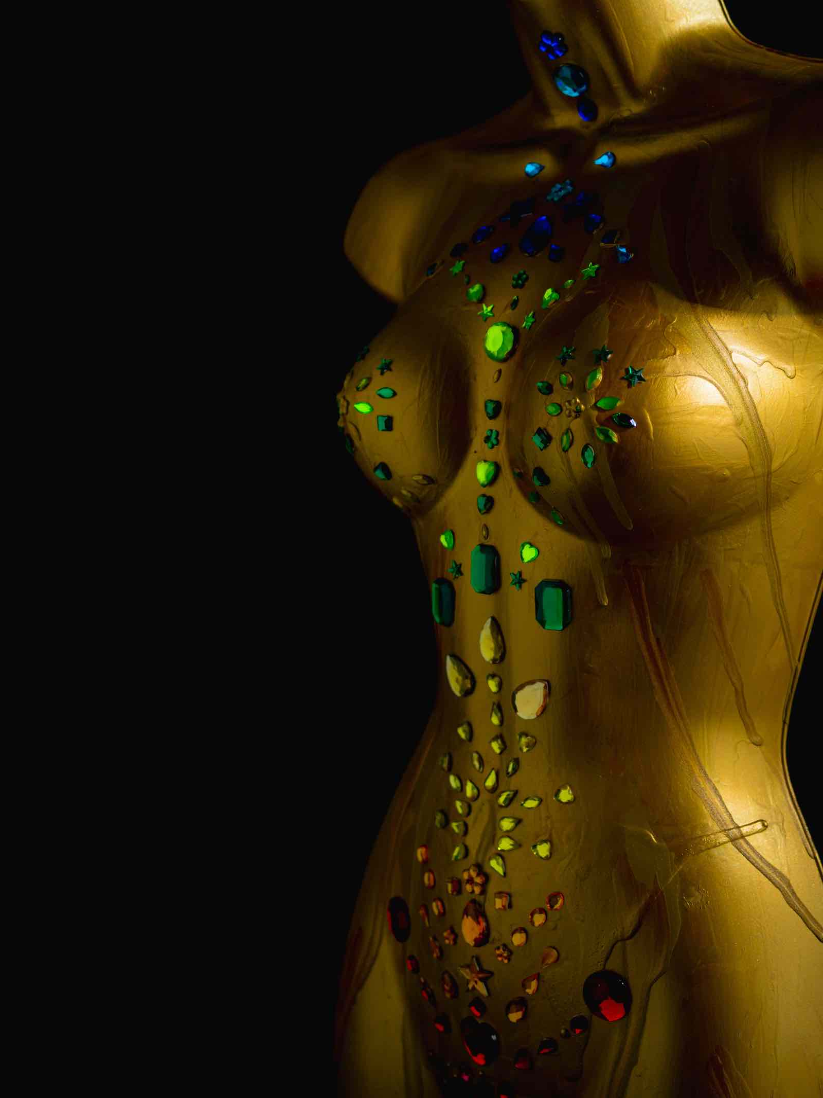A golden woman's figure is adorned with gems colored with the colors of the chakras.